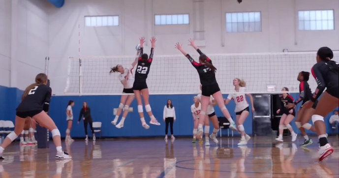 Volleyball players jump to block the ball.