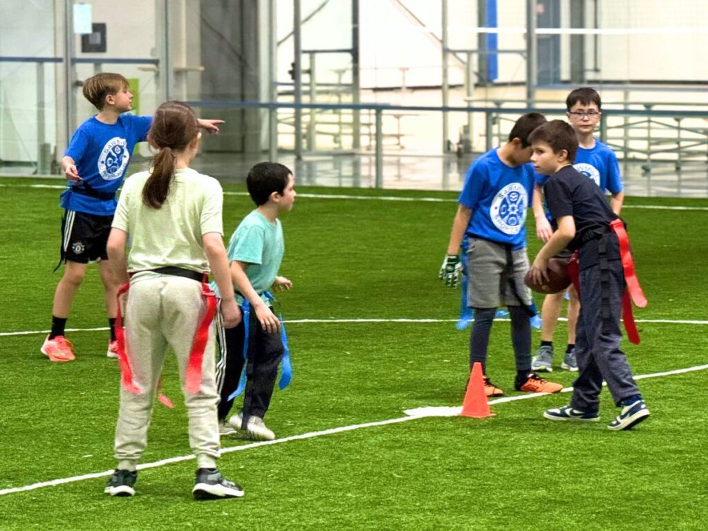 A group of young athletes play flag football on the turf at Sawmill Sports Hub.