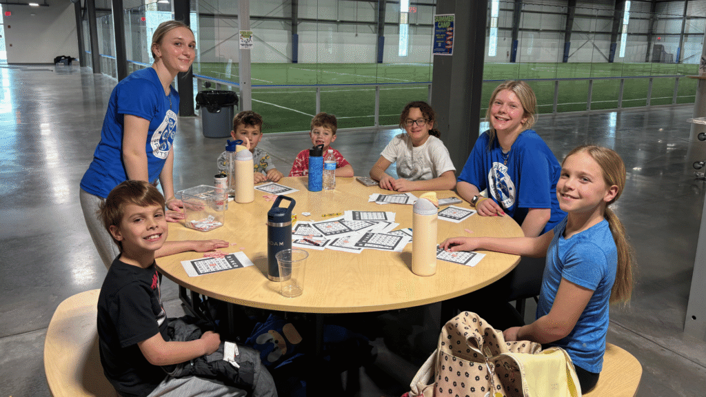 Happy children at a school day off camp at Sawmill Sports Hub. They are smiling with their camp counselors. They are working on an art and craft project.