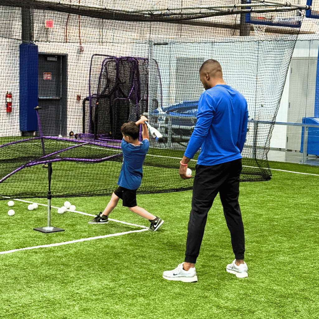 This image shows the interior of a modern batting cage facility, part of the Sawmill baseball and t-ball programs. The space features a vibrant green indoor turf and is enclosed by protective netting. It is a dedicated space for athletes to train and improve their skills, embodying the spirit of dedication and practice within the world of baseball
