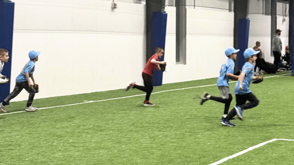Kids in baseball uniforms running on the expansive turf field at Sawmill Sports Hub in Willowbrook, IL.