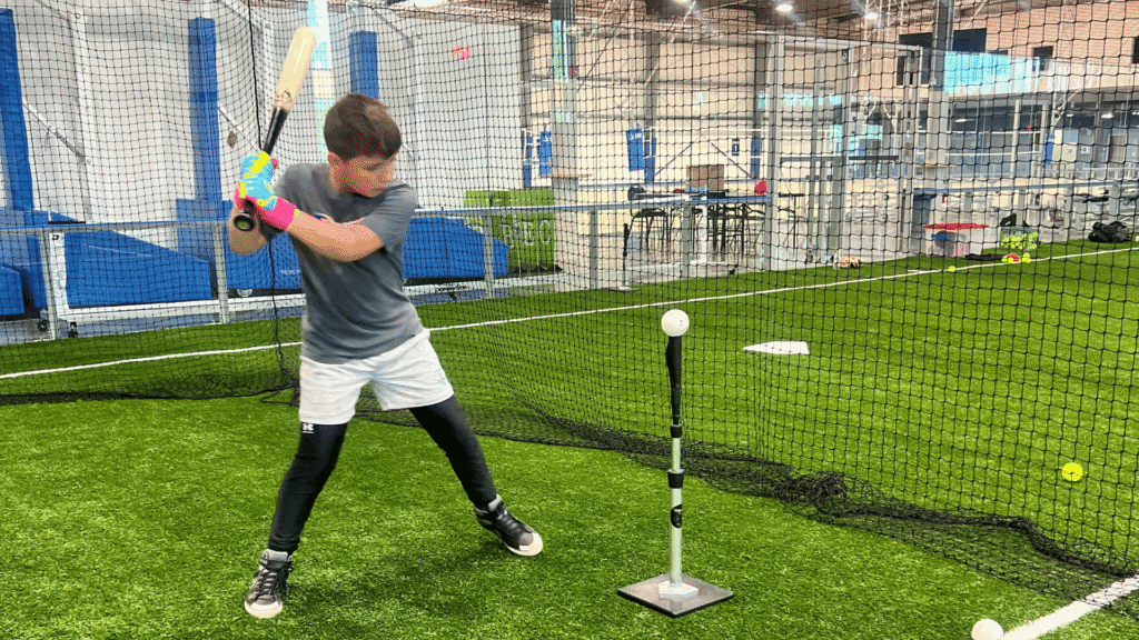 A young baseball player hits a ball in a batting cage a Sawmill Sports Hub.